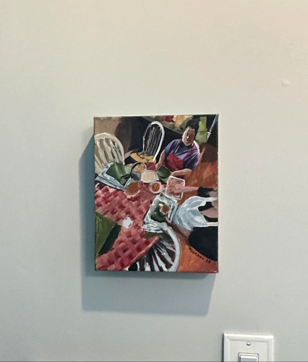 A small colorful painting depicting a table scene with people and objects, mounted on a light gray wall next to a teal door frame.